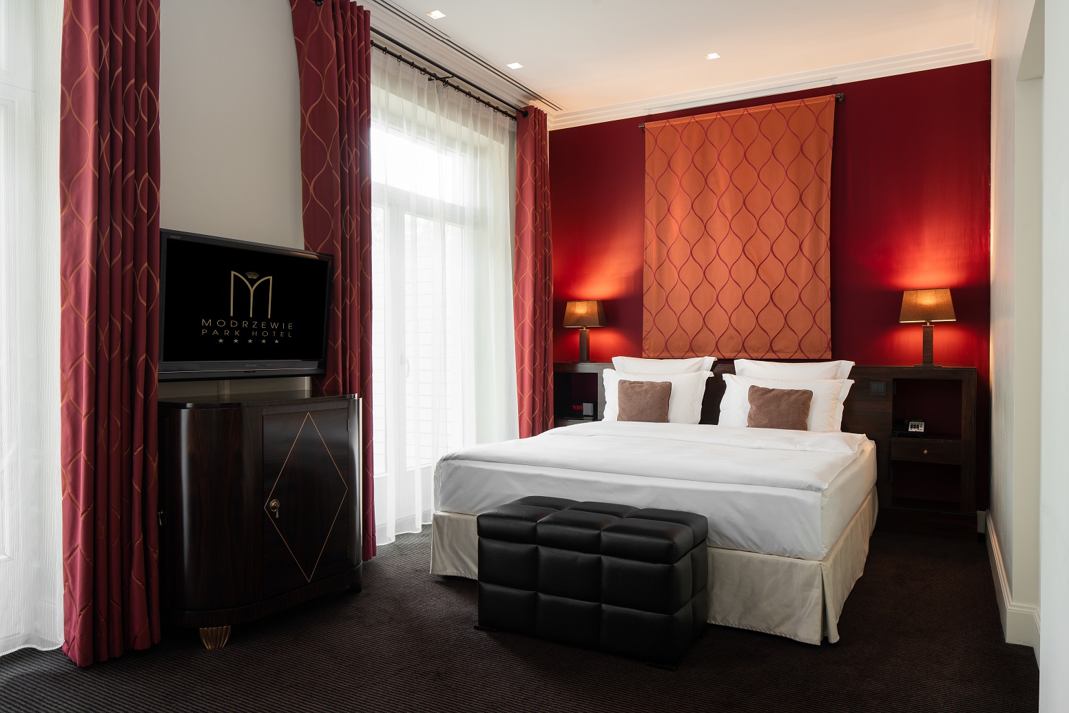zdjęcie przedstawia hotelowy pokój, urządzony gustownie w kolorach bieli czerwieni i mocnego brązu